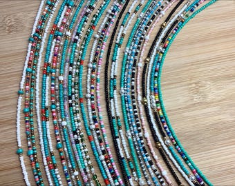Puede incluir: Una colección de collares de cuentas en varios colores, incluyendo turquesa, blanco, negro y dorado. Los collares están dispuestos en forma de abanico, mostrando el intrincado trabajo de cuentas y las diversas paletas de colores. Las cuentas parecen pequeñas y delicadas, creando una exhibición texturizada y visualmente atractiva.