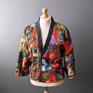 May include: A colorful patchwork jacket with a black collar and button closure. The jacket is displayed on a wooden mannequin.
