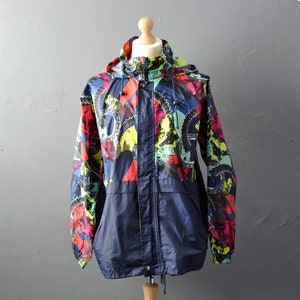 Puede incluir: Una chaqueta azul marino con capucha con un estampado abstracto colorido que presenta formas geométricas y engranajes. La chaqueta tiene una cremallera y un cordón en la cintura.