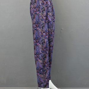 May include: Purple, pink, and black paisley print pants. The pants are on a white mannequin and have a wide leg.