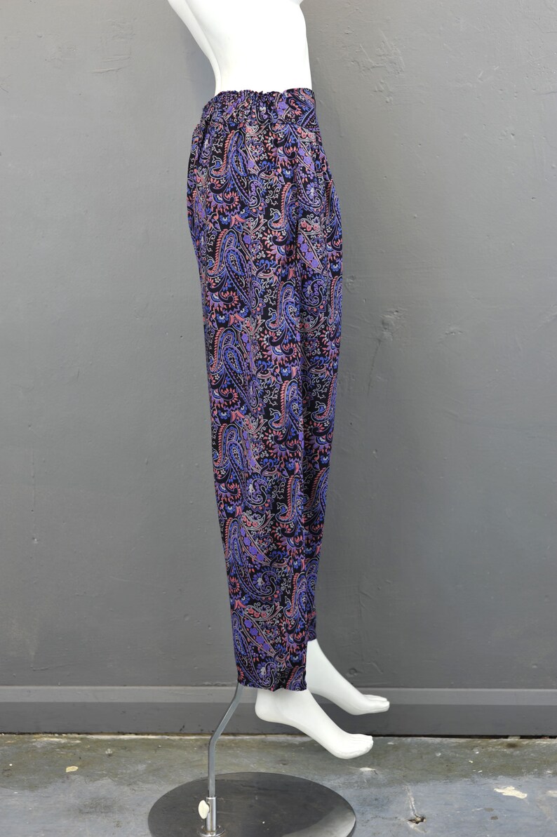May include: Purple, pink, and black paisley print pants. The pants are on a white mannequin and have a wide leg.