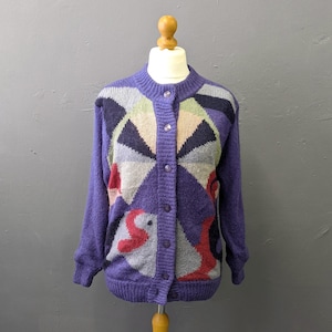 Peut inclure: Un cardigan en tricot violet avec un motif géométrique dans des tons bleu foncé, vert clair, gris et rouge. Le vêtement présente une encolure ronde, des manches longues, des poignets et un ourlet côtelés, ainsi qu'une fermeture boutonnée.