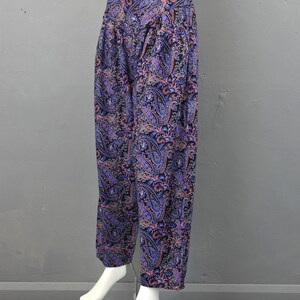 May include: Purple, pink, and black paisley print pants. The pants are wide-legged and have a loose fit.