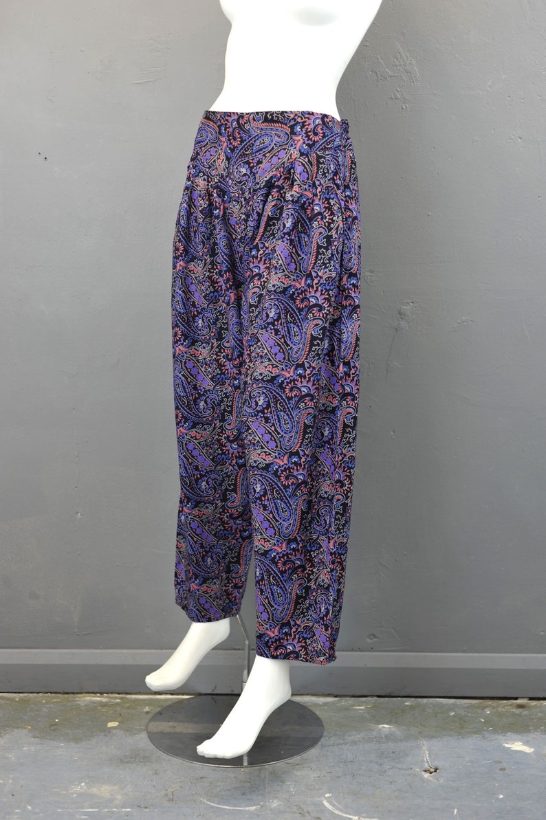 May include: Purple, pink, and black paisley print pants. The pants are wide-legged and have a loose fit.