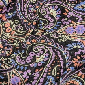 May include: Close-up of a black fabric with a paisley pattern in shades of pink, purple, and blue.