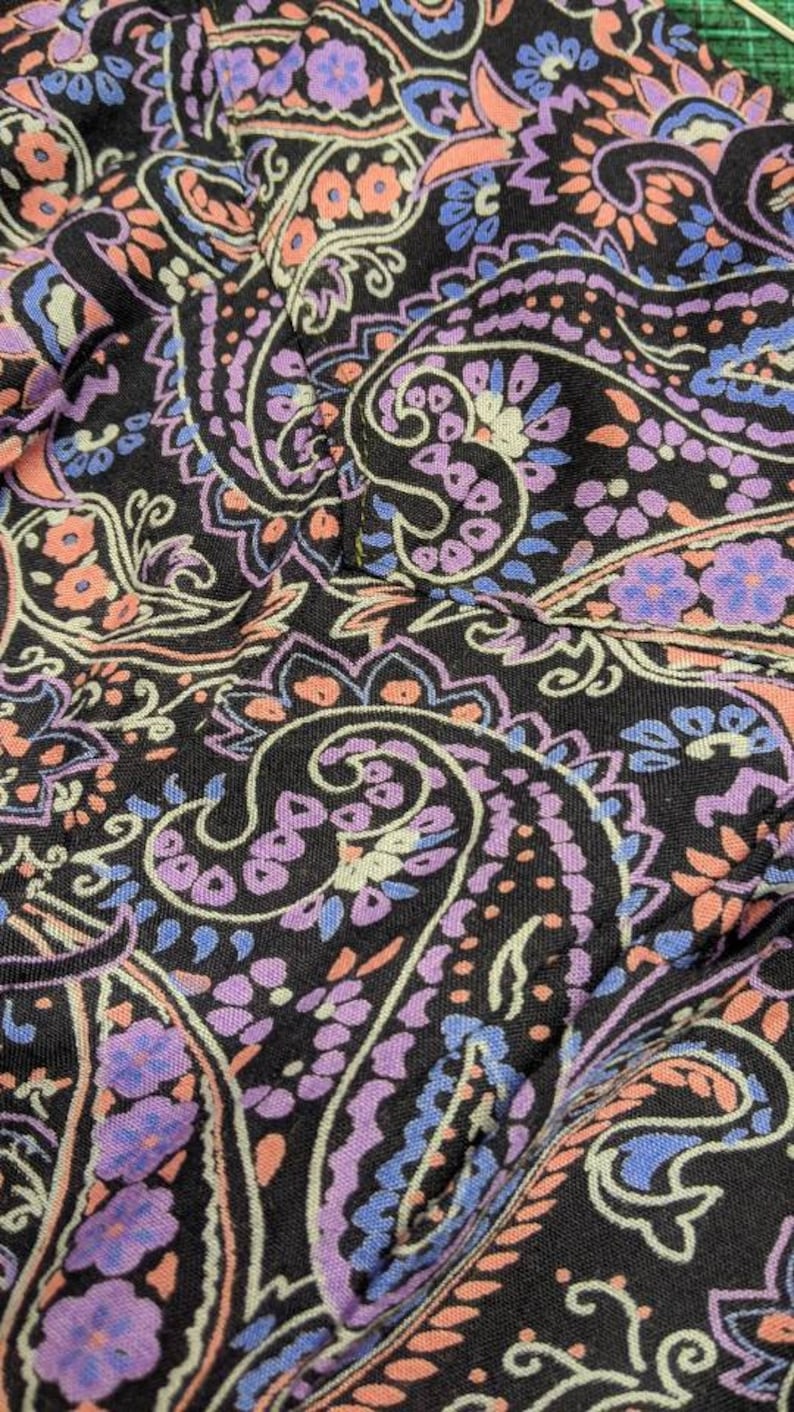 May include: Close-up of a black fabric with a paisley pattern in shades of pink, purple, and blue.