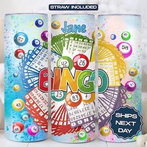 May include: A personalized tumbler with a colorful bingo theme. The tumbler features a large "BINGO" word with colorful letters and a variety of bingo balls and cards. The tumbler is personalized with the name "Jane".