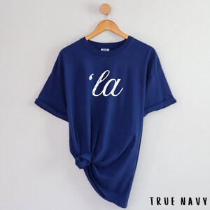 May include: A navy blue t-shirt with a white graphic that says 'la' in a cursive font.