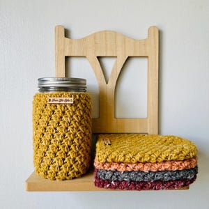 May include: A white ceramic mug with a black handle and the text "But First, Coffee" in a bold, black font. The mug is set against a blurred background, suggesting a cozy setting.