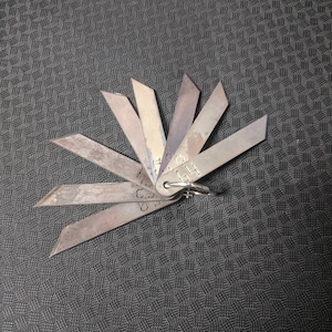 Peut inclure: Un ensemble de sept lames de jauge en métal avec un anneau pour attacher à un porte-clés. Les lames sont étiquetées avec différentes tailles, notamment 0,015, 0,020, 0,025, 0,030, 0,035, 0,040 et 0,045.