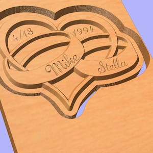 May include: A wooden plaque featuring two intertwined rings in the shape of a heart. The rings are engraved with the names "Mike" and "Stella" and the date "4/13/1994".