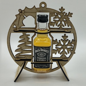 May include: A wooden Christmas ornament shaped like a snowflake with a small bottle of Jack Daniel's Tennessee Whiskey inside. The ornament has a stand to display it.
