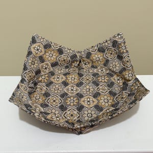 May include: A square fabric bowl with a floral pattern in shades of brown, gray, and tan. The bowl is open at the top and has a folded design. The fabric has a repeating geometric design.
