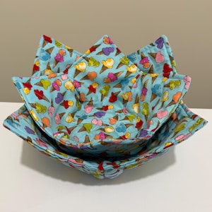 May include: Three nesting fabric bowls with a light blue background and a colorful ice cream cone pattern. The bowls are square with folded corners, creating a star-like shape. The ice cream cones are in various colors.