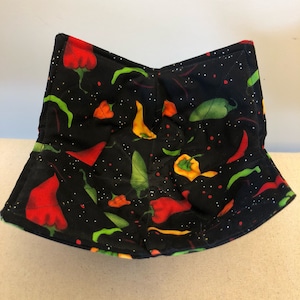 May include: Black quilted hot pad with a pattern of red, yellow, and green peppers on a black background.