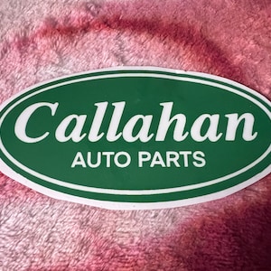 May include: An oval sticker with a green background and white border. The text "Callahan AUTO PARTS" is displayed in white, with "Callahan" in a larger, cursive font above "AUTO PARTS".