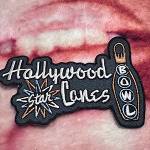 May include: Embroidered patch featuring the text "Hollywood Bowl Lanes" in white script, with a star graphic and a bowling pin design. The patch has a dark gray background with gold and light blue accents.
