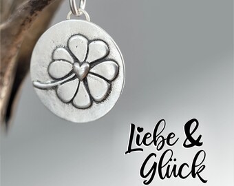 Op de afbeelding: Zilveren bedel met een klavertje vier met een hart in het midden. De bedel is gegraveerd met de woorden "Liebe & Glück", wat in het Nederlands "Liefde & Geluk" betekent.