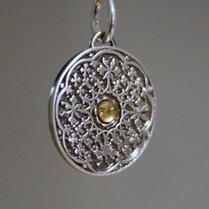 Könnte beinhalten: Eine silberne Halskette mit einem runden, filigranen Anhänger, der in der Mitte einen kleinen goldenen Kreis hat.