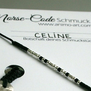 Peut inclure: Un bracelet en cordon noir avec des perles argentées qui épellent le nom "CELINE" en code Morse. Le bracelet est présenté sur une carte blanche avec le texte "Morse-Code Schmuck" et "www.animo-art.com". La carte comprend également un tableau de l'alphabet Morse.