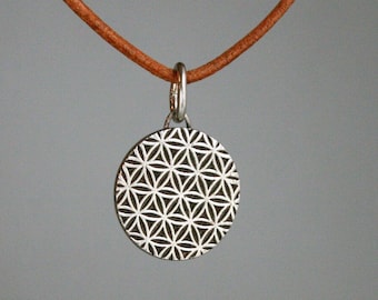 May include: A silver necklace with a round pendant featuring a geometric flower of life design. The necklace is on a brown leather cord.