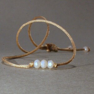 Può includere: Una collana semplice con un cordoncino beige e tre perline bianche.