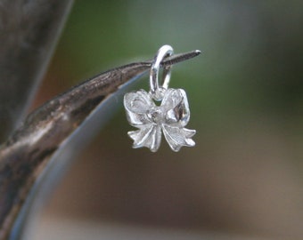 May include: A silver charm in the shape of a bow. The bow is detailed and has a loop at the top for attaching to a necklace or bracelet.