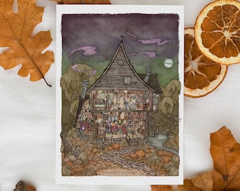 May include: An illustrated card depicts a detailed, multi-story house with figures inside, under a night sky. The card is surrounded by fall foliage, including orange oak leaves, dried orange slices, acorns, and a dried rose, all arranged on a white surface.