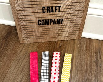 May include: Four key fobs with different patterns: a textured pink, a black and white grid, red polka dots, and yellow chevron. Each has a metal ring and a clasp. A wooden sign with the text "WESTWARD CRAFT COMPANY" is in the background.