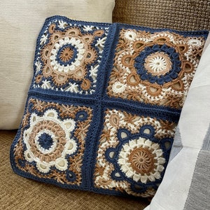 May include: A square crocheted pillow with a blue background and four beige and white crocheted squares with intricate designs.