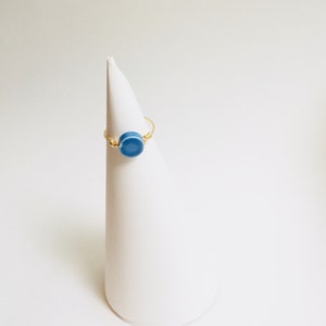 May include: A gold ring with a blue ceramic circle. The ring is displayed on a white cone.