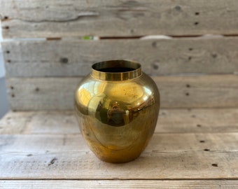 May include: A shiny gold metal vase with a rounded body. The vase is sitting on a wooden surface.