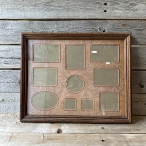 May include: A rectangular, multi-photo frame with a dark brown wooden frame. The frame holds various sized openings, including squares, rectangles, and an oval. The background is a light brown with a subtle pattern.