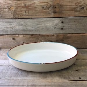 May include: White oval ceramic baking dish with a brown and blue rim. The dish is sitting on a wooden surface.
