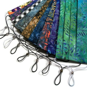 May include: A collection of colorful fabric face masks with black and white elastic straps and silver bead toggles. The masks are arranged in a fan shape with the straps extending out from the bottom.