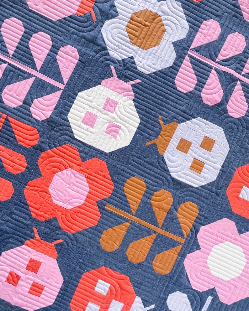 Puede incluir: Una colcha con fondo azul y varias formas en rosa, blanco, naranja y marr&oacute;n. Las formas incluyen flores, mariquitas y hojas.