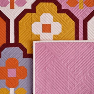 May include: A quilted fabric with a geometric pattern in shades of orange, yellow, white, pink, and burgundy. The fabric has a diamond-shaped quilting pattern.