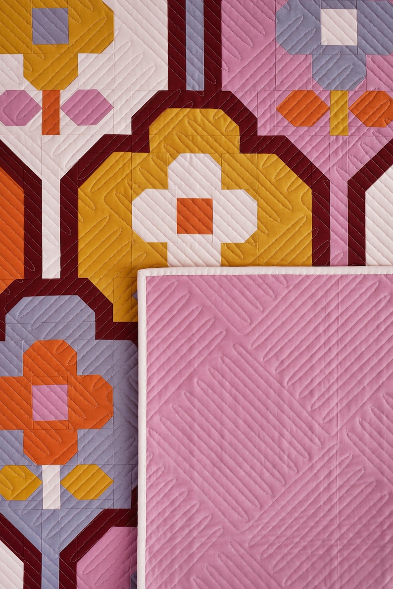 May include: A quilted fabric with a geometric pattern in shades of orange, yellow, white, pink, and burgundy. The fabric has a diamond-shaped quilting pattern.