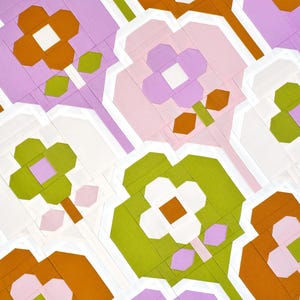 Op de afbeelding: Een herhalend patroon van abstracte bloemen in tinten roze, groen, wit en oranje. De bloemen zijn gemaakt van geometrische vormen en zijn in een verspringend patroon gerangschikt.