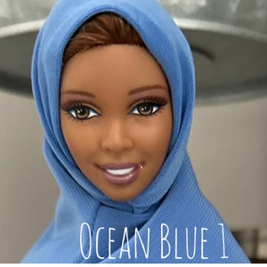 May include: A doll with brown hair wearing a blue hijab. The text "OCEAN BLUE 1" is written below the doll.