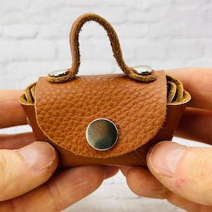 May include: A small brown leather purse with a top handle and silver metal accents. The purse is closed and has a flap with a silver metal button.