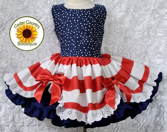 Può includere: Un vestito per bambini a tema patriottico, con un corpetto blu navy ricoperto di stelle bianche. La gonna presenta strisce rosse e bianche, fiocchi rossi e una balza blu navy. Il vestito è per bambini.