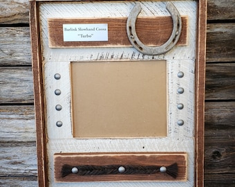 Puede incluir: Un marco de fotos de madera rústico con un acabado blanqueado. El marco tiene una herradura, una tira de cuero trenzada y una placa de metal que dice "Bartlink Slowhand Coosa "Turbo"".