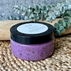 May include: A purple lavender and grapefruit sugar scrub in a clear jar with a black lid. The jar is labelled "Lavender & Grapefruit Sugar Scrub".