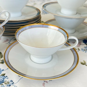 May include: A set of white teacups and saucers with a blue and gold trim. The cups and saucers are stacked on top of each other.