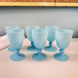 May include: Set of six light blue glass goblets with a fluted design. The goblets have a round base and a stem.