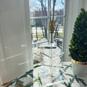 May include: A clear acrylic table lamp with a stacked design. The lamp has a gold metal base and a white cord.