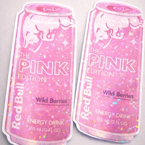 May include: Two pink Red Bull "The Pink Edition" stickers. The stickers feature a glittery design with the text "Wild Berries" and "Energy Drink 355 ml (12 FL OZ)". The Red Bull logo is visible on the can.