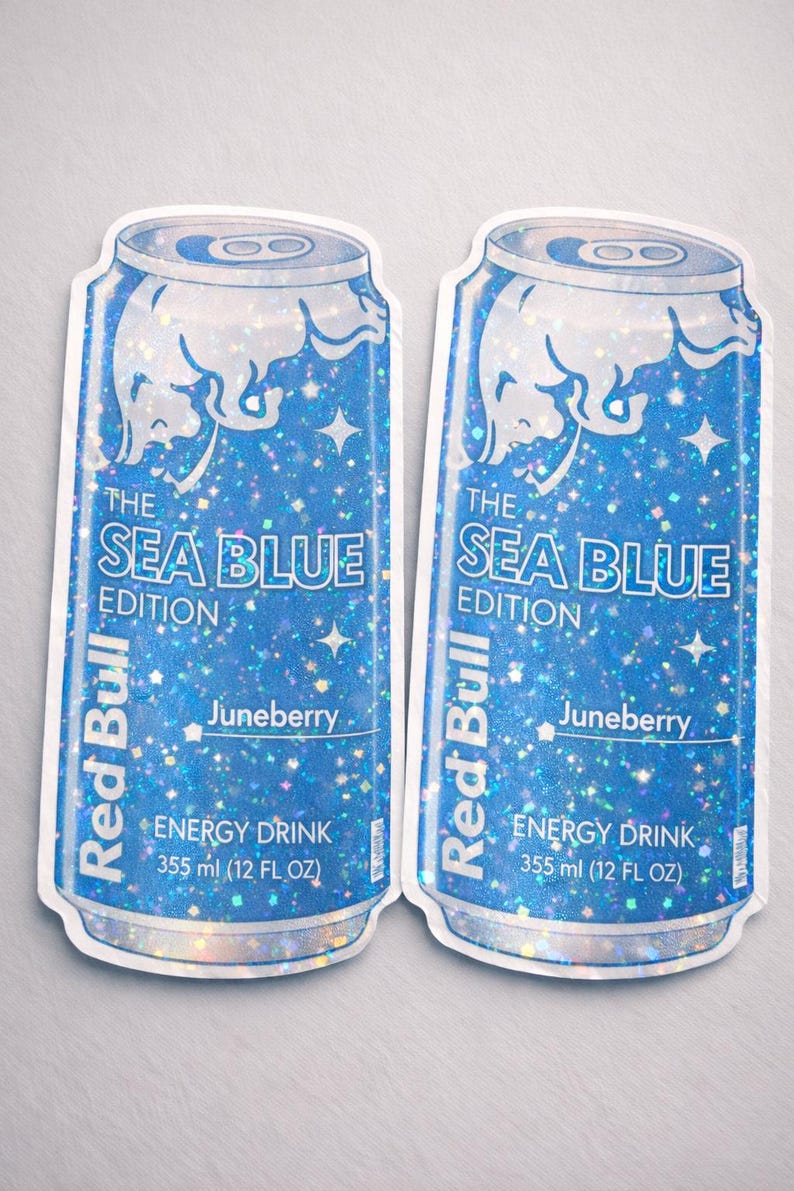 May include: Two stickers of Red Bull's Sea Blue Edition energy drink cans. The cans are blue with a glittery effect and feature the Red Bull logo, the flavor "Juneberry", and the text "ENERGY DRINK 355 ml (12 FL OZ)".