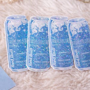 May include: Four stickers of Red Bull energy drink cans. The stickers are blue with glitter and feature the text "The Sea Blue Edition" and "Juneberry". Each can is 355 ml (12 fl oz).